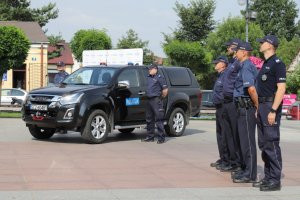 policjanci stoją po dwóch stronach nowego czarnego nieoznakowanego radiowozu terenowego ISUZU