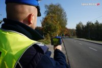policjant stoi przy drodze z radarem w ręku i mierzy prędkość przejeżdżających samochodów