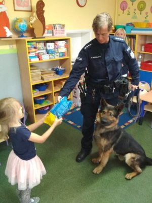 policjant z psem policyjnym, dziewczynka wręcza paczkę karmy