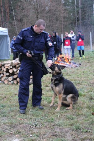 policjant z psem w tle ognisko i stojace osoby