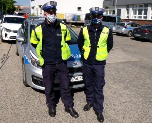 policjanci z ruchu drogowego stoją w kamizelkach odblaskowych i białych czapkach przed radiowozem