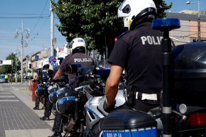 Policjanci na motocyklach służbowych tyłem do fotografującego stoją na środku pasażu pieszo-rowerowego w alejach