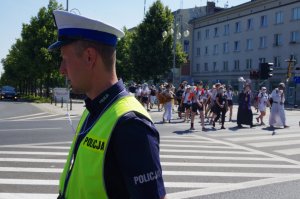 policjant ruchu drogowego w białej czapce i gwizdkiem kieruje ruchem, pielgrzymi przechodzą po przejściu dla pieszych