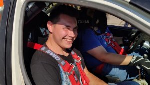 uśmiechnięty chłopak - uczestnik akcji siedzi na przednim fotelu pasażera w samochodzie rajdowym