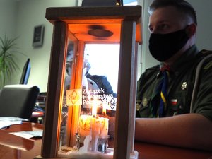 Komendant siedzi przy biurku na przeciwko harcerze, na stole stoi lampion