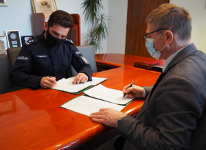 policjant siedzi przy stole na przeciwko dyrektora szkoły i podpisują dokumenty