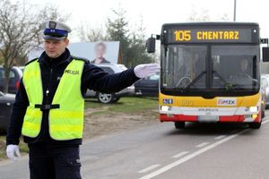 Policjant na drodze kieruje ruchem, za nim stoi autobus
